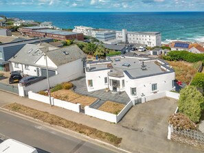 A coastal residential area with a white building featuring a flat roof and a small garden. - 5 Bed in Newquay (oc-p00894) (Newquay)