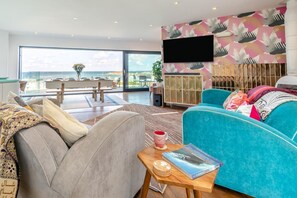 A modern living room with a large window, a sofa, a coffee table, and a television. - 5 Bed in Newquay (oc-p00894) (Newquay)