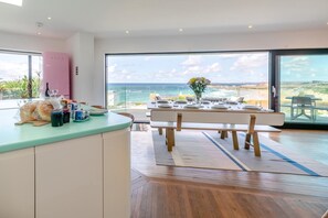 A modern kitchen with a view of the ocean, a dining area set for a meal, and a large window. - 5 Bed in Newquay (oc-p00894) (Newquay)
