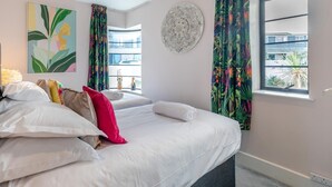 Ein Hotelzimmer mit Bett, Kissen, einem Wandbild, einem Fenster mit Vorhängen und einer dekorativen Wandplatte.