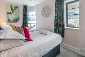 Hotelkamer met een bed, kussens, een kunstwerk aan de muur, een raam met gordijnen en een decoratief wandbord.