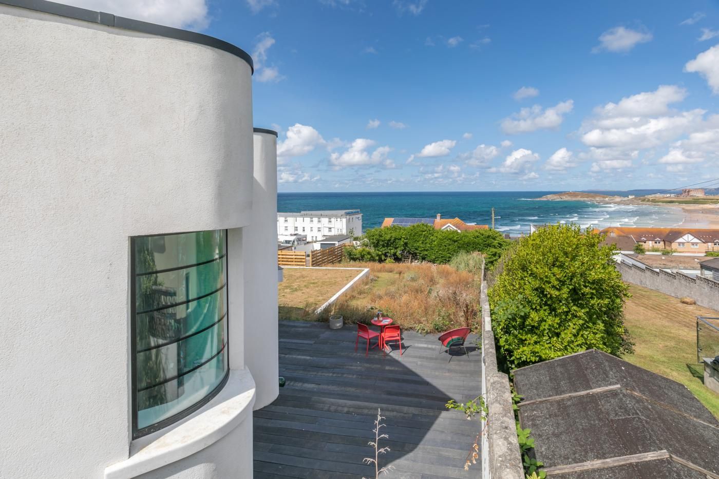 A residential building with a view of the sea and a garden area with red chairs.