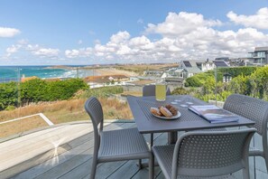 A deck with a table and chairs overlooking a coastal view. - 5 Bed in Newquay (oc-p00894) (Newquay)
