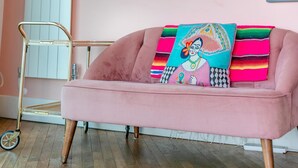 Ein rosafarzenes Sofa mit farbigem Kissen und ein Metallwagen in einem Raum mit Holzboden.