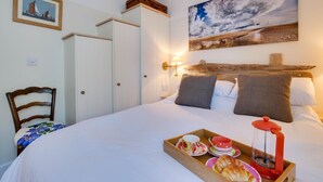 Un dormitorio con cama, cabecera de madera, un cuadro, una silla y una bandeja con alimentos para el desayuno.