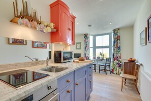 A modern kitchen with a red cabinet, a microwave, and a dining area with a table and chairs. - 1 Bed in St. Ives (oc-34belm) (Saint Ives)