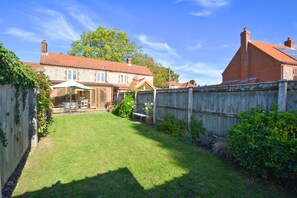 A backyard with a lawn, a wooden fence, and a brick house with a tiled roof. - 3 Bed in North Creake (oc-1916) (North Creake)
