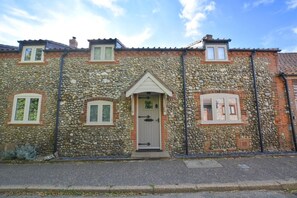 A stone facade building with a central entrance, two windows on either side, and a small dormer window above. - 3 Bed in North Creake (oc-1916) (North Creake)
