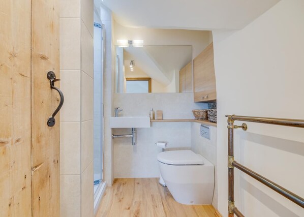 A compact bathroom with a wooden door, a white toilet, a sink, and a shower area.