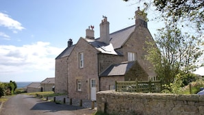 A stone house with a paved driveway and a stone wall on one side. - 1 Bed in Alnwick (oc-nb312) (Embleton)