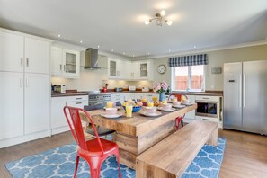 A modern kitchen with white cabinets, a wooden dining table, and a red chair. - 5 Bed in Seahouses (oc-nb621) (Seahouses)