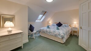 Une chambre à coucher comprenant un lit, un bureau, une chaise, une commode et une lucarne.