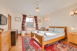 A bedroom with a wooden bed, a dresser, a radiator, a window with curtains, a wall-mounted TV, and a nightstand with a lamp. - 2 Bed in Chatton (oc-nb620) (Chatton)