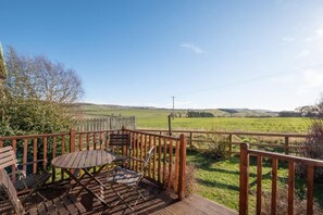 A wooden deck with a table and chairs, overlooking a grassy field and hills. - 2 Bed in Chatton (oc-nb620) (Chatton)
