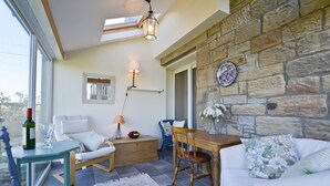 A cozy room with a stone wall, a wooden table, a white sofa, and a glass table with a bottle and glass. - 2 Bed in Morpeth (oc-nb596) (Low Hauxley)