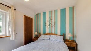 Een slaapkamer met een bed, twee nachtkastjes, een raam met gordijnen en een wand met verticale strepen.