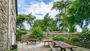 Een stenen gebouw met een terras en houten picknicktafels en banken.