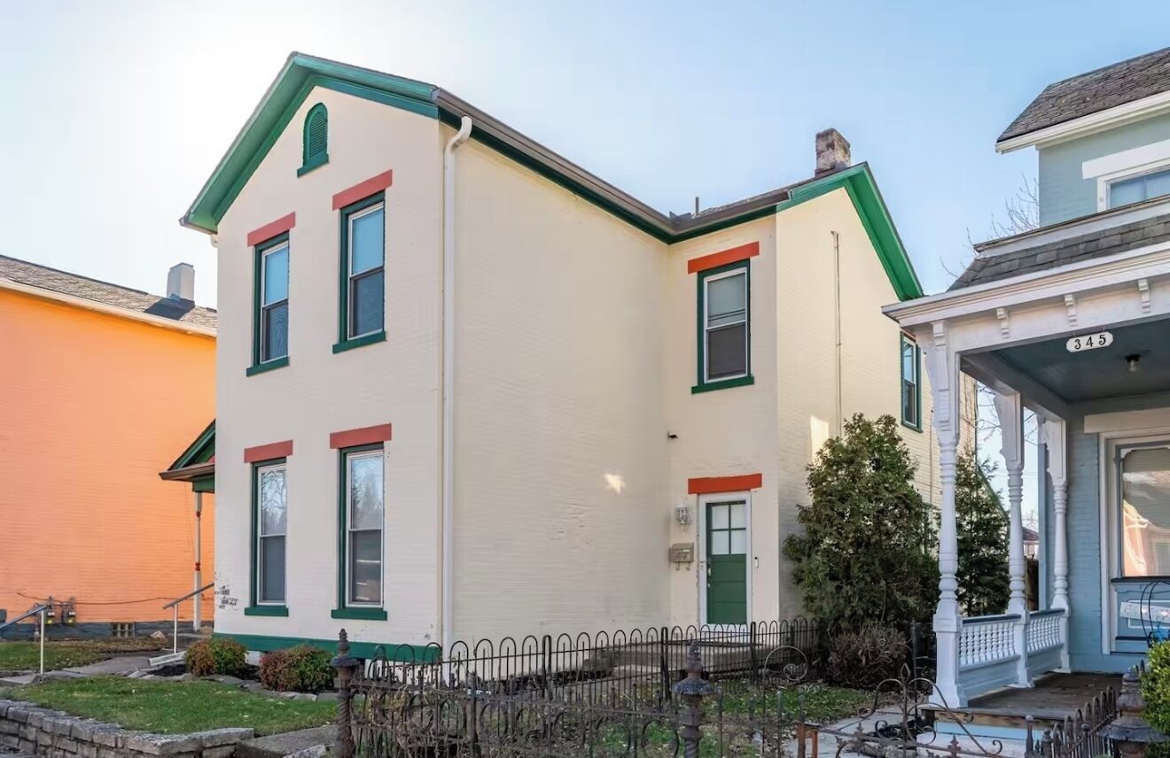 Une maison à deux étages, avec une façade verte et blanche, un porche à l’avant et le numéro « 345 » sur le côté.