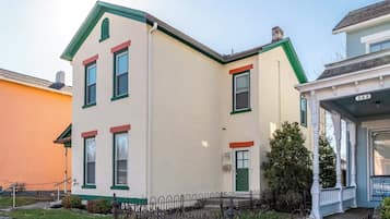 Une maison à deux étages, avec une façade verte et blanche, un porche à l’avant et le numéro « 345 » sur le côté.