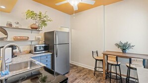 A compact kitchen with a refrigerator, microwave, and sink. There is a ceiling fan and a small table with chairs. - Historic south park gem - close to UD, MVH & more. (Dayton)