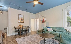 A living room with a green sofa, a dining table with chairs, a ceiling fan, and a painting on the wall.