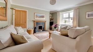 A living room with a fireplace, a sofa, a chair, and a large window. - 4 Bed in Wooler (oc-nb344) (Kirknewton)
