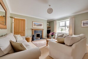 A living room with a fireplace, a sofa, a chair, and a large window. - 4 Bed in Wooler (oc-nb344) (Kirknewton)