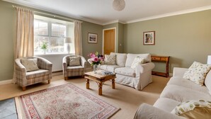 A living room with a sofa, armchairs, a coffee table, a rug, and a window with curtains. - 4 Bed in Wooler (oc-nb344) (Kirknewton)