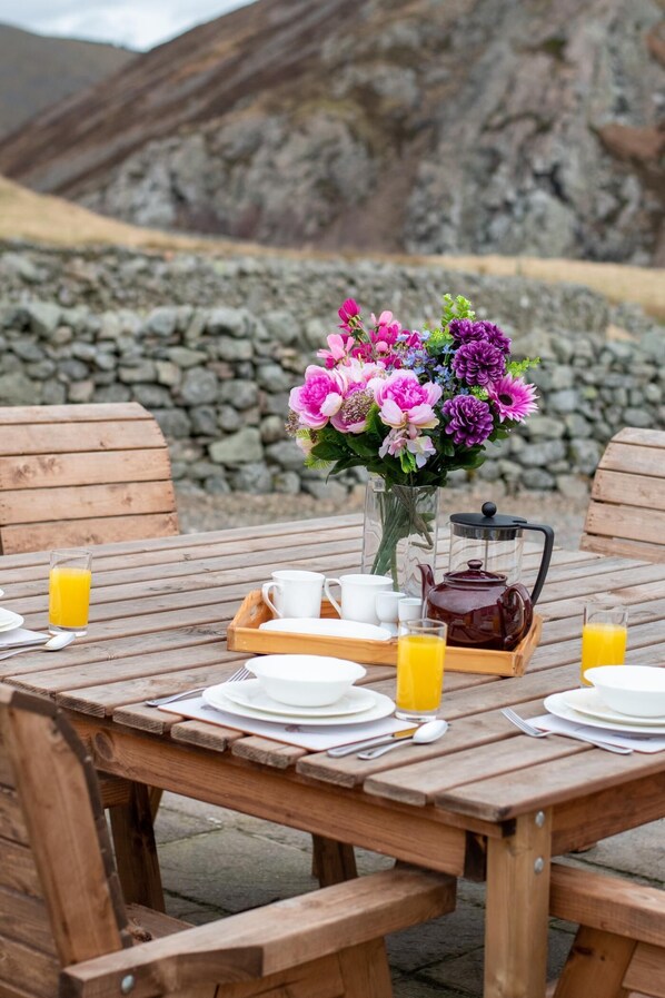 A wooden table set for breakfast with a vase of flowers, a teapot, cups, and glasses of orange juice. - 4 Bed in Wooler (oc-nb344) (Kirknewton)