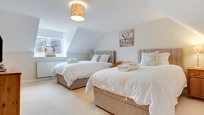 A bedroom with two beds, a window, a radiator, a lamp, and a painting on the wall. - 4 Bed in Wooler (oc-nb344) (Kirknewton)