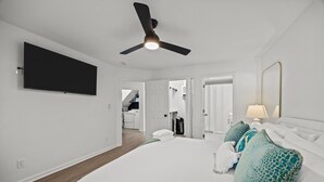 Et moderne hotelværelse med en stor seng, ventilator, fladskærms-TV og et badeværelse, der kan ses igennem en åben dør.