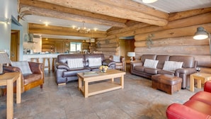 A log cabin interior with a living area featuring leather sofas, a wooden coffee table, and a kitchen in the background. - 4 Bed in Alston (oc-nb575) (Alston Moor)