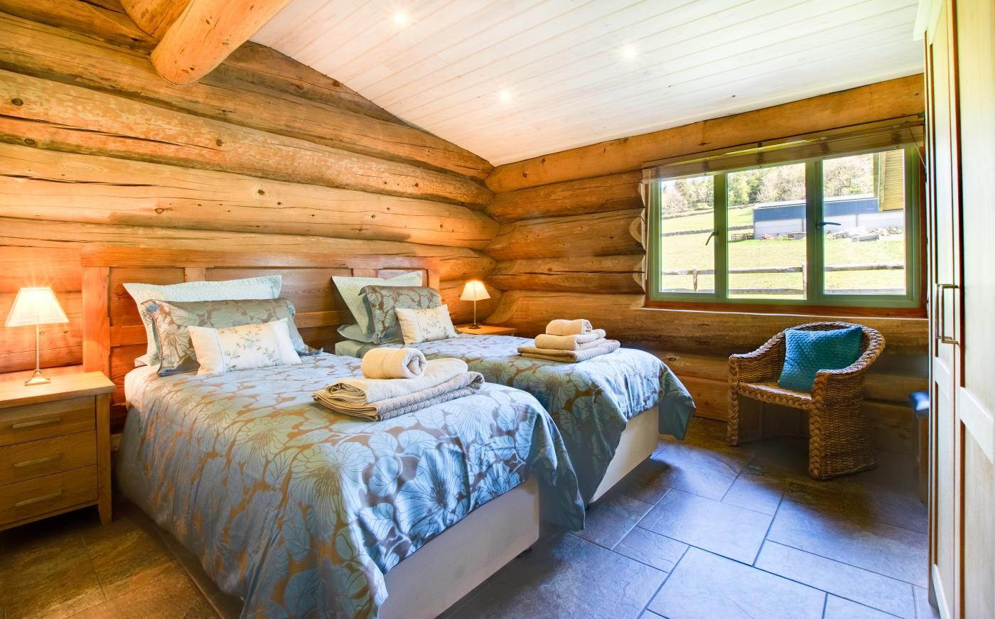Une chambre dans un chalet en rondins, avec deux lits, une chaise et une fenêtre.