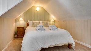 A cozy attic bedroom with a sloped ceiling, a wooden nightstand, a lamp, and neatly folded towels on the bed. - 2 Bed in Wooler (oc-nb317) (Kirknewton)