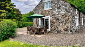 A stone house with a patio, outdoor seating, and a green umbrella. - 2 Bed in Wooler (oc-nb396) (Kirknewton)