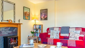 Ein gemütliches Wohnzimmer mit Kamin, einem roten Sofa mit Zierkissen, einem Bücherregal und einer Lampe.
