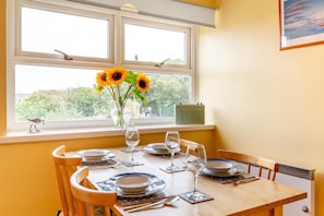 Ein Esstisch für zwei Personen, gedeckt mit Tellern, Gläsern und einer Vase mit Sonnenblumen an einem Fenster.