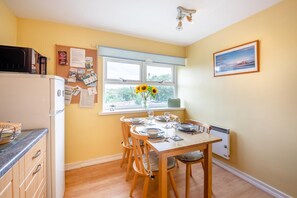 Een kleine keuken met een eettafel voor vier personen, een raam met uitzicht en een aan de muur hangend schilderij.