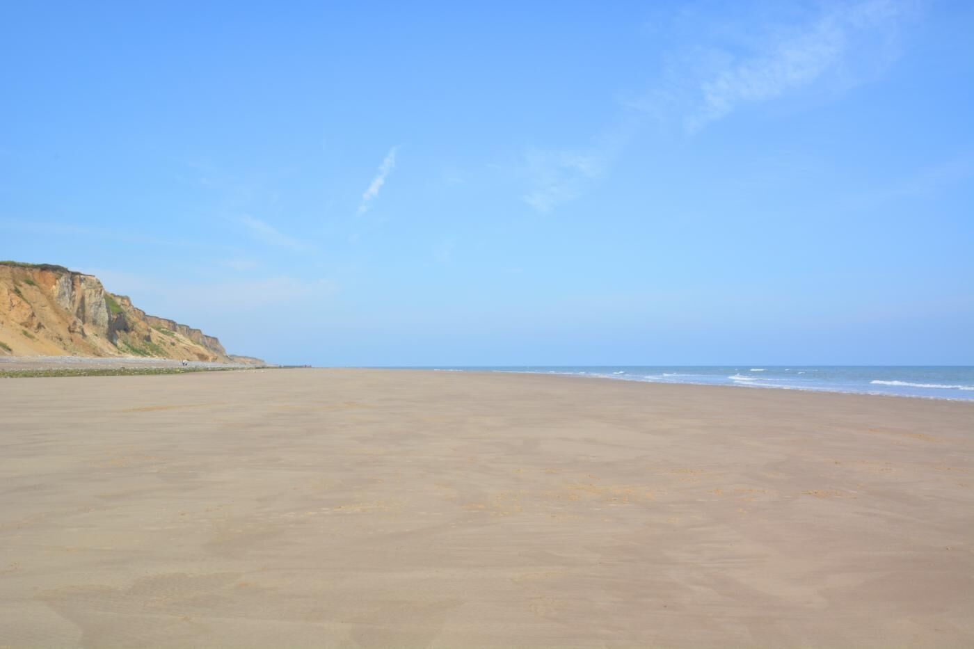 A wide, sandy beach with gentle waves and a cliff on the left.