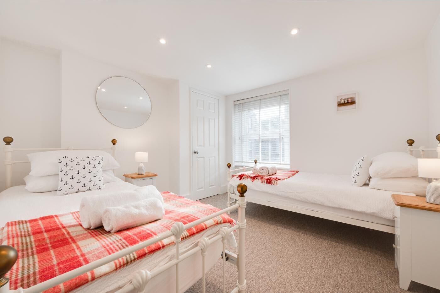 Een schone, witte kamer met twee bedden, een grote spiegel en een raam met zonwering.