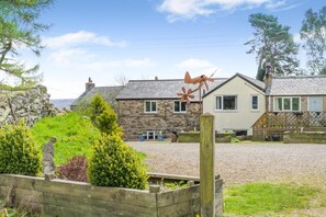 A stone house with a gravel driveway, a wooden fence, and a windmill in the foreground. - 1 Bed in Haltwhistle (oc-nb556) (Haltwhistle)