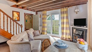 A cozy living room with a sofa, a dining table with plates and a bowl, a fireplace, and a television. - 1 Bed in Haltwhistle (oc-nb556) (Haltwhistle)