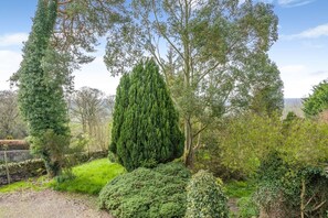 A garden with various trees and shrubs, a stone wall, and a view of the landscape. - 1 Bed in Haltwhistle (oc-nb556) (Haltwhistle)