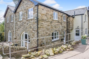 A stone building with multiple windows, a visible door, and a small garden area with potted plants. - 3 Bed in Haltwhistle (oc-nb558) (Haltwhistle)