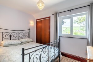 Une chambre à coucher avec un lit, une porte en bois, une fenêtre donnant sur un beau paysage et un lustre.