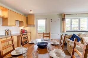 Un coin repas avec une table en bois dressée pour quatre personnes, une cuisine avec des placards en bois et une vue par la fenêtre.