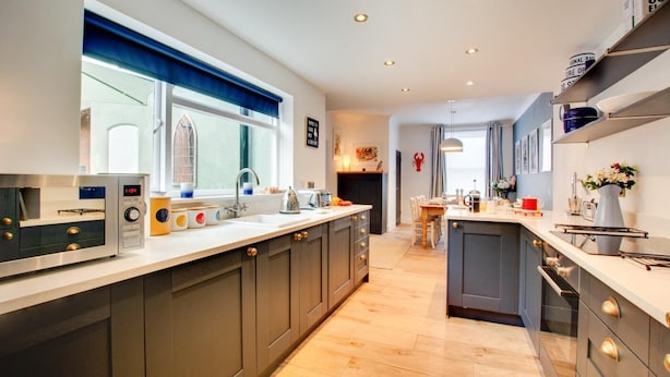 A modern kitchen with a built-in oven, a dining area with a table and chairs, and a small island with a sink. - 3 Bed in Cromer (oc-1927) (Cromer)