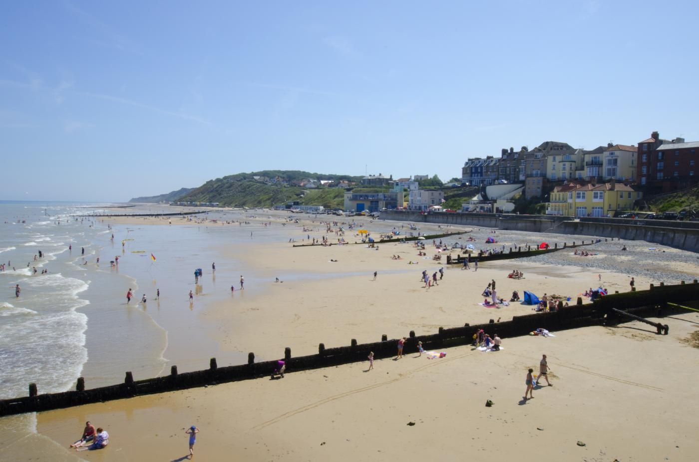 A beach with people, a sea wall, and buildings in the background.