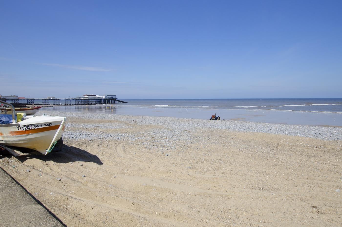 Uma praia com um cais, um barco e uma pessoa na água.