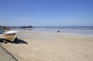 A beach with a pier, a boat, and a person in the water. - 3 Bed in Cromer (oc-1927) (Cromer)